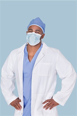 Portrait of an African American male surgeon with hands on hips over light blue background Stock Photo - Premium Royalty-Free, Code: 693-06379074