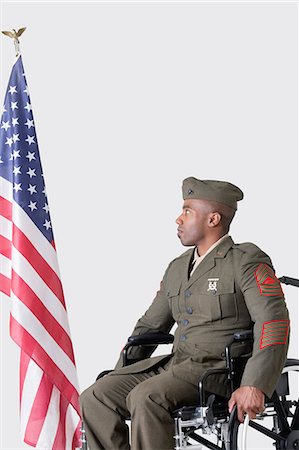 Young soldier in wheelchair looking at American flag over gray background Stock Photo - Premium Royalty-Free, Code: 693-06379161
