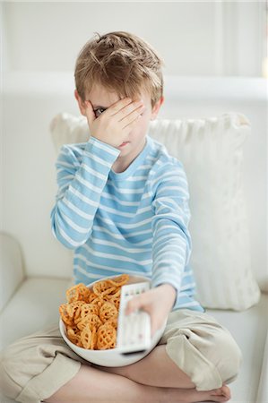 Little boy watching scary movie with a bowl full of wheel shape snack pellets Stock Photo - Premium Royalty-Free, Code: 693-06379389