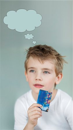 Pensive little boy holding credit card with speech bubble over gray background Stock Photo - Premium Royalty-Free, Code: 693-06379424