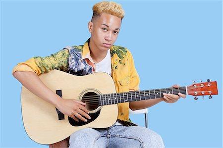 Portrait of a young teenage boy playing guitar over blue background Stock Photo - Premium Royalty-Free, Code: 693-06379584