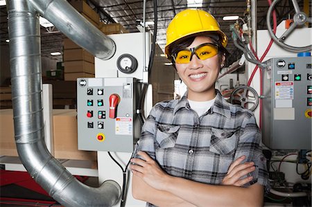 simsearch:693-06379747,k - Portrait of female industrial worker smiling while standing in factory with machines in background Stock Photo - Premium Royalty-Free, Code: 693-06379665