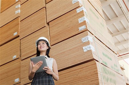 simsearch:693-06379747,k - Low angle view of female industrial worker holding tablet PC with stacked wooden planks in background Stock Photo - Premium Royalty-Free, Code: 693-06379670