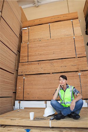 simsearch:693-06379747,k - Pensive female industrial worker sitting cross-legged on wooden planks Stock Photo - Premium Royalty-Free, Code: 693-06379684