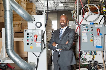 simsearch:693-06379747,k - Portrait of African American businessman standing arms crossed with machinery in background Stock Photo - Premium Royalty-Free, Code: 693-06379757