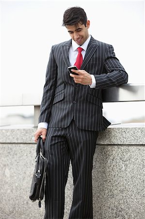 parapet - Young Indian businessman texting through cell phone while holding laptop bag at parapet Stock Photo - Premium Royalty-Free, Code: 693-06379796