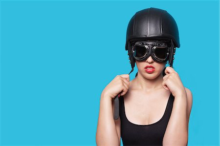 Young woman wearing nostalgic helmet and goggles against blue background Stock Photo - Premium Royalty-Free, Code: 693-06379858