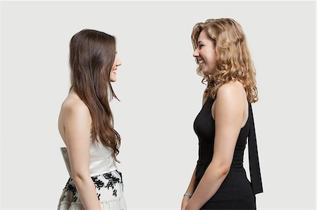 Two female friends looking at each other and smiling over gray background Stock Photo - Premium Royalty-Free, Code: 693-06380031