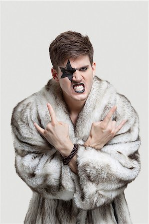 fur - Portrait of frustrated young man in fur coat clenching teeth and making rebellious gesture against gray background Stock Photo - Premium Royalty-Free, Code: 693-06380070