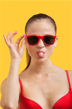 Portrait of young woman in sunglasses sticking out tongue over yellow background Foto de stock - Sin royalties Premium, Código: 693-06403267