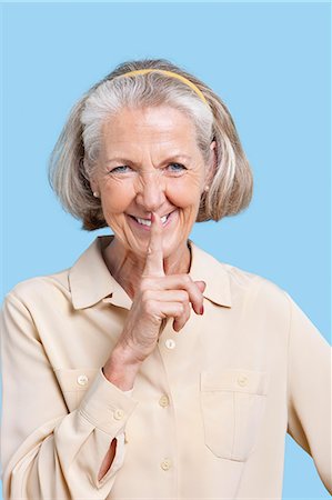 shhh - Portrait of smiling senior woman in casuals with finger on lips against blue background Stock Photo - Premium Royalty-Free, Code: 693-06403400