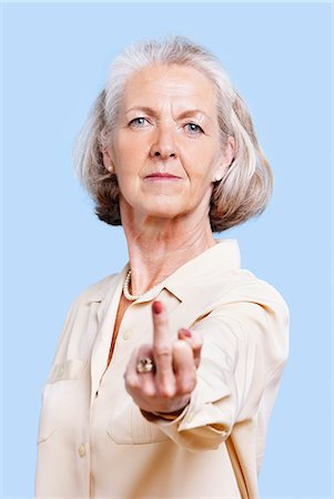 scorn - Senior woman in casuals making rebellious hand gesture against blue background Stock Photo - Premium Royalty-Free, Code: 693-06403480
