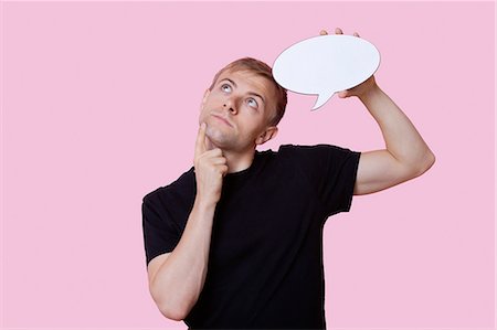 speech - Thoughtful young man holding speech bubble while looking up over pink background Stock Photo - Premium Royalty-Free, Code: 693-06403534