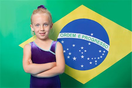 Portrait of a happy young female gymnast with arms crossed standing in front of Brazilian flag Stock Photo - Premium Royalty-Free, Code: 693-06403562