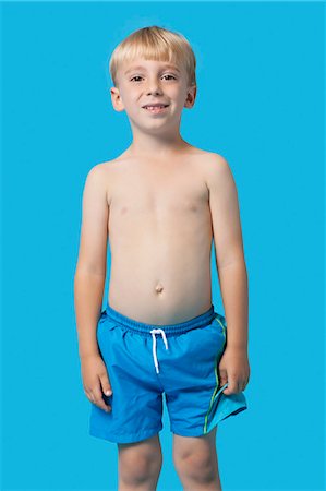 Portrait of a happy young boy in swim trunks over blue background Stock Photo - Premium Royalty-Free, Code: 693-06403576