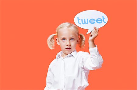 Portrait of a young girl holding tweet bubble against orange background Stock Photo - Premium Royalty-Free, Code: 693-06403591