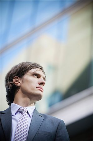 Low angle view of young businessman looking away with building in the background Stock Photo - Premium Royalty-Free, Code: 693-06435817