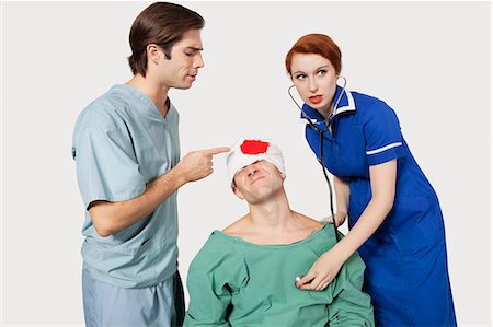 Male doctor with female nurse examining an injured patient against gray background Stock Photo - Premium Royalty-Free, Code: 693-06435913