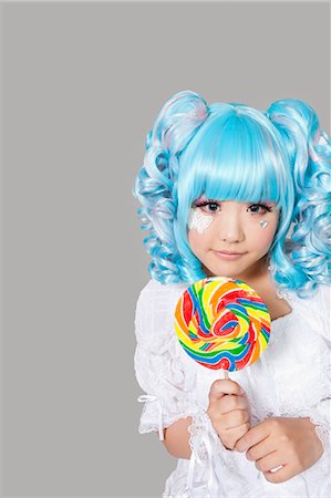 simsearch:693-06435933,k - Portrait of cute young woman dressed as a doll holding lollipop over gray background Stock Photo - Premium Royalty-Free, Code: 693-06436013