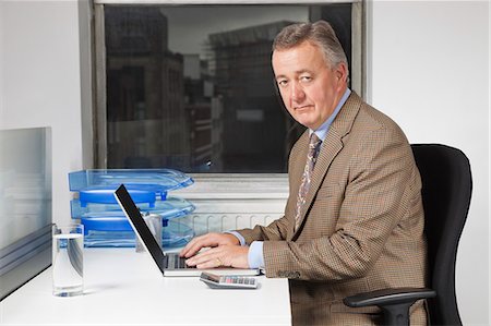 Portrait of middle-aged businessman using laptop at desk in office Stock Photo - Premium Royalty-Free, Code: 693-06497631