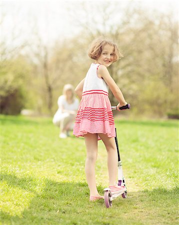 scooter rear view - Young girl riding scooter through park with mother in background Stock Photo - Premium Royalty-Free, Code: 693-06967423