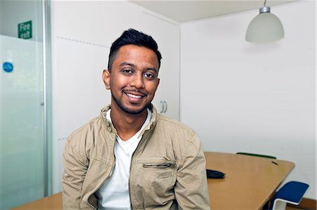 Young Indian man smiling at camera in his office Stock Photo - Premium Royalty-Free, Code: 693-06967523