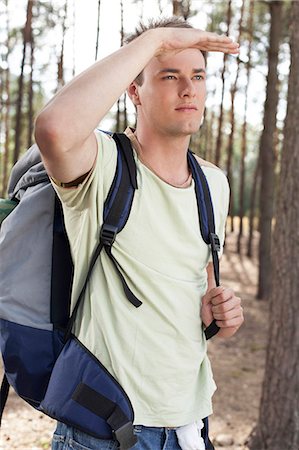 Young man with backpack shielding eyes in forest Stock Photo - Premium Royalty-Free, Code: 693-07444479