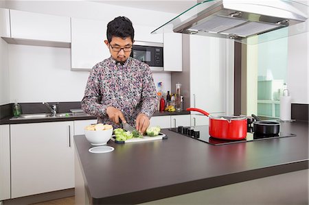 Young man cutting broccoli at kitchen counter Stock Photo - Premium Royalty-Free, Code: 693-07455849