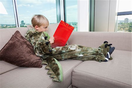 dinosaur - Boy in dinosaur costume reading story book on sofa at home Stock Photo - Premium Royalty-Free, Code: 693-07455873