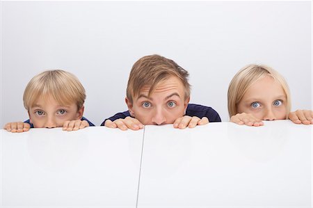 surprised kids - Father and children peeking over table Stock Photo - Premium Royalty-Free, Code: 693-07455886