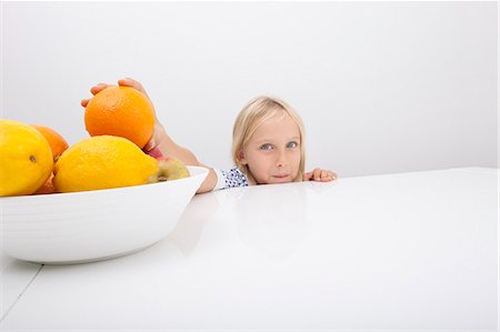 Portrait of little girl holding orange from fruit bowl Foto de stock - Sin royalties Premium, Código: 693-07455882