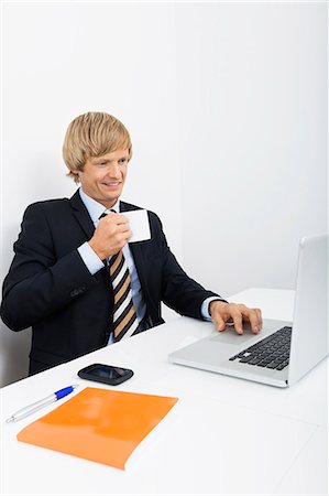 Confident businessman having coffee white using laptop in office Stock Photo - Premium Royalty-Free, Code: 693-07455974