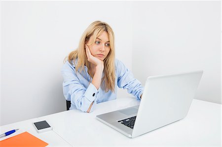 Bored young businesswoman using laptop at desk in office Stock Photo - Premium Royalty-Free, Code: 693-07455977