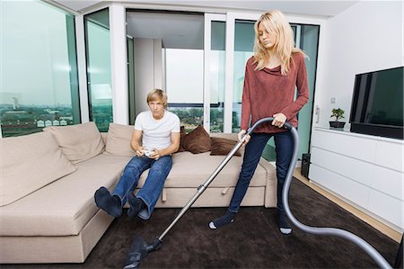 Woman vacuuming while man play video game in living room at home Foto de stock - Sin royalties Premium, Código: 693-07456042