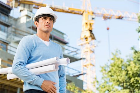 Male architect holding rolled up blueprints while standing at construction site Foto de stock - Sin royalties Premium, Código: 693-07456147