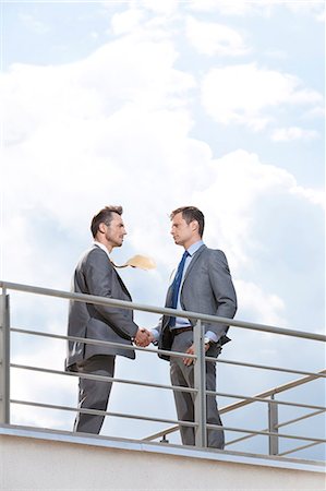 Side view of businessmen shaking hands at terrace railings against sky Stock Photo - Premium Royalty-Free, Code: 693-07456191