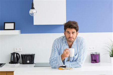 simsearch:693-07456416,k - Portrait of young ill man holding coffee mug while leaning on kitchen counter Foto de stock - Sin royalties Premium, Código: 693-07456337