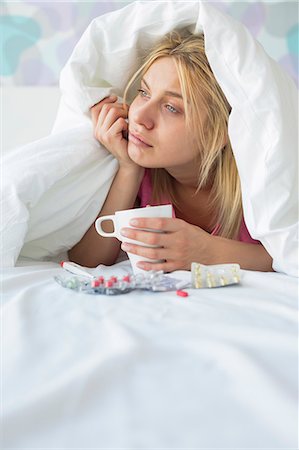 simsearch:693-07456416,k - Young woman with coffee mug and medicines suffering from fever while covered in quilt on bed Foto de stock - Sin royalties Premium, Código: 693-07456382