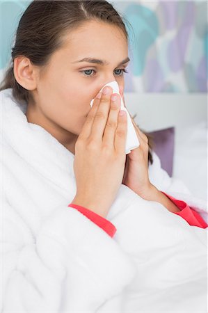 Young woman suffering from cold blowing nose in bedroom Stock Photo - Premium Royalty-Free, Code: 693-07456396