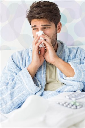 Sick man blowing his nose in tissue paper on bed at home Stock Photo - Premium Royalty-Free, Code: 693-07456405