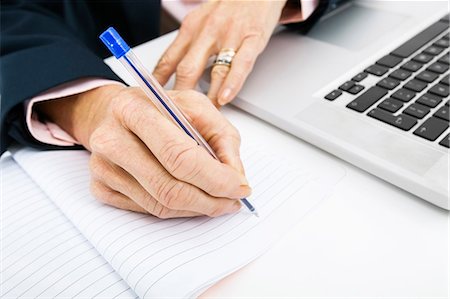 Cropped image of businesswoman with laptop writing in book on office desk Stock Photo - Premium Royalty-Free, Code: 693-07456477