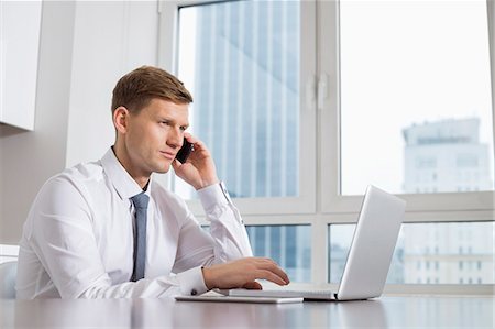 simsearch:693-07542313,k - Mid adult businessman on call while using laptop at home Stock Photo - Premium Royalty-Free, Code: 693-07542226