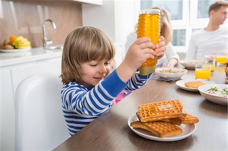 foods on table - Happy boy pouring honey on waffles while having breakfast with family Stock Photo - Premium Royalty-Free, Code: 693-07542220