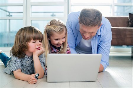 Happy father with children using laptop on floor in living room Stock Photo - Premium Royalty-Free, Code: 693-07542237