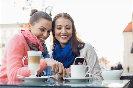 Happy female friends using cell phone at sidewalk cafe Stock Photo - Premium Royalty-Free, Code: 693-07542309