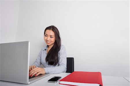 Happy young businesswoman using laptop at office desk Stock Photo - Premium Royalty-Free, Code: 693-07542358