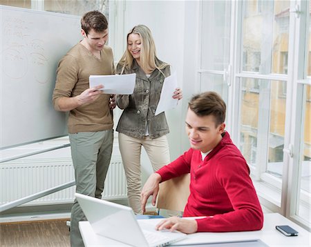 personal computer - Businessman using laptop while coworkers discussing over documents in office Stock Photo - Premium Royalty-Free, Code: 693-07672563