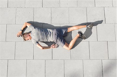 High angle view of tired sporty man lying on tiled sidewalk Photographie de stock - Premium Libres de Droits, Code: 693-07672609