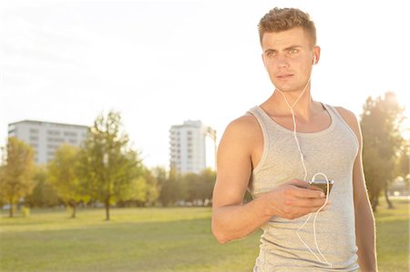simsearch:693-07672615,k - Young jogger looking away while listening music through cell phone in park Stock Photo - Premium Royalty-Free, Code: 693-07672614
