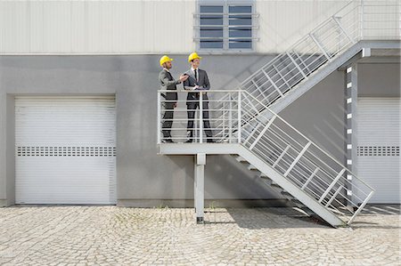 suit talking - Young male architects with clipboard discussing on stairway Stock Photo - Premium Royalty-Free, Code: 693-07672625